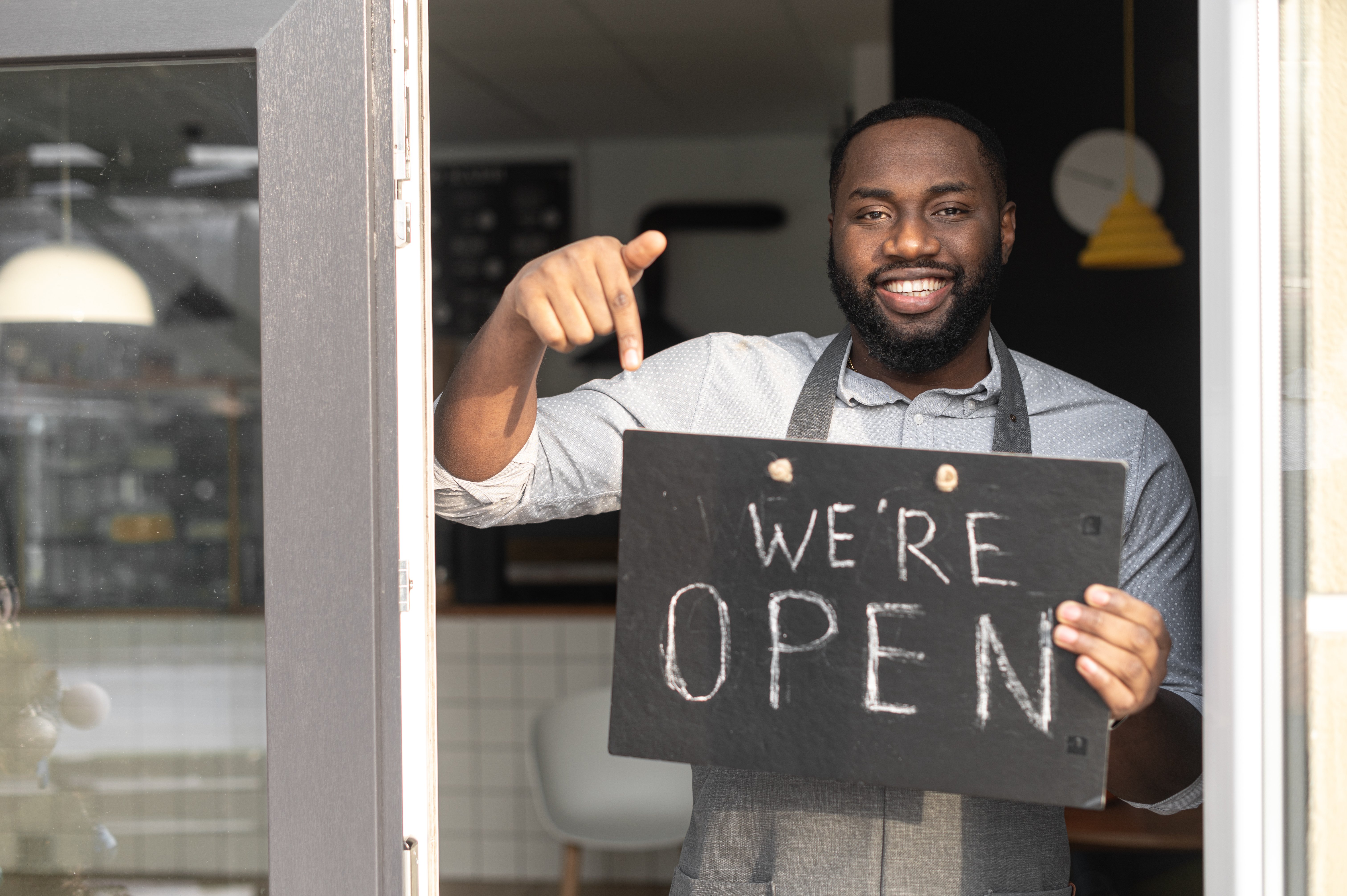 Man standing in the doorway holding a "we're open" sign 