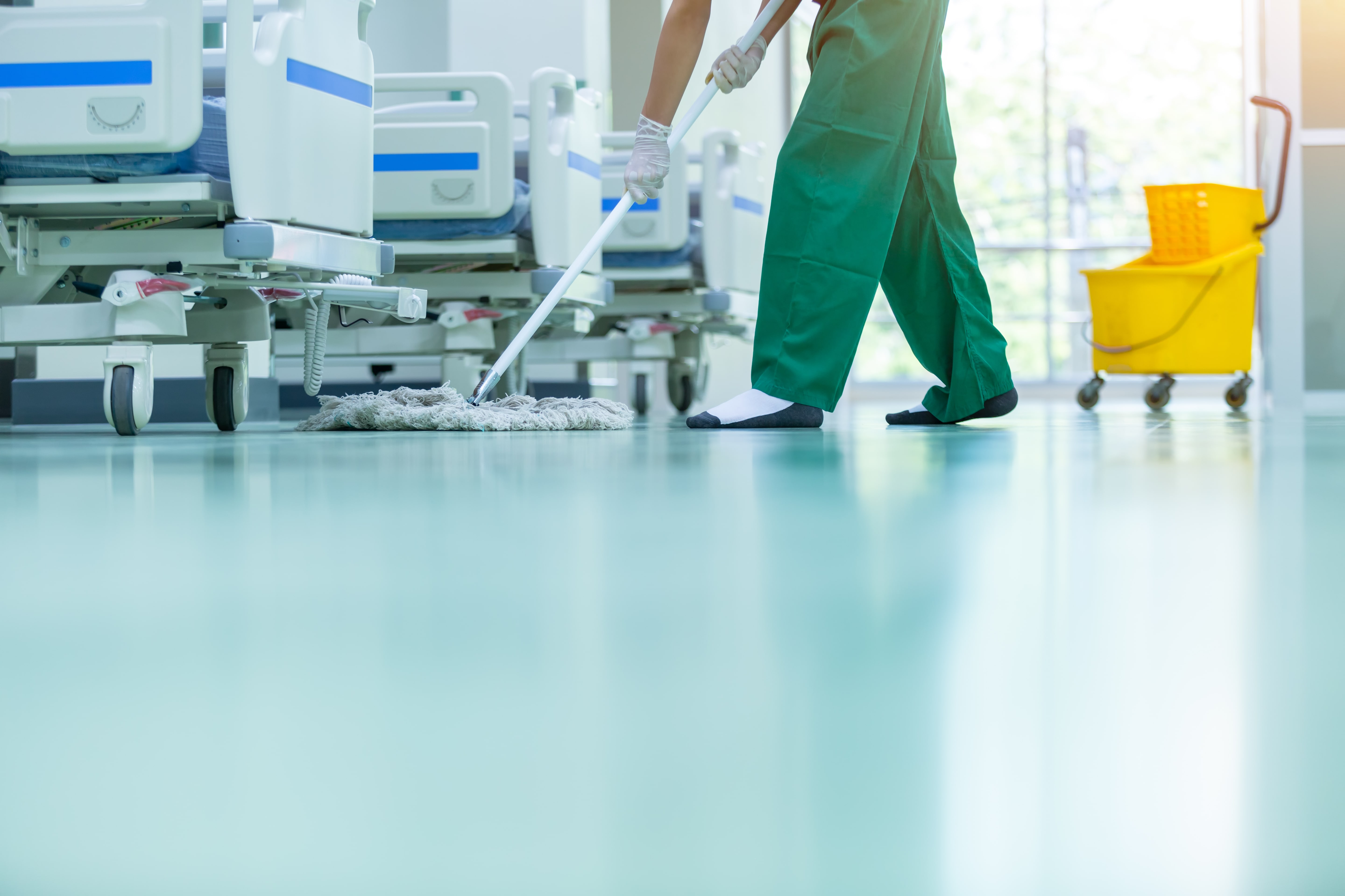 EVS professional mopping medical facility floor around  hospital beds