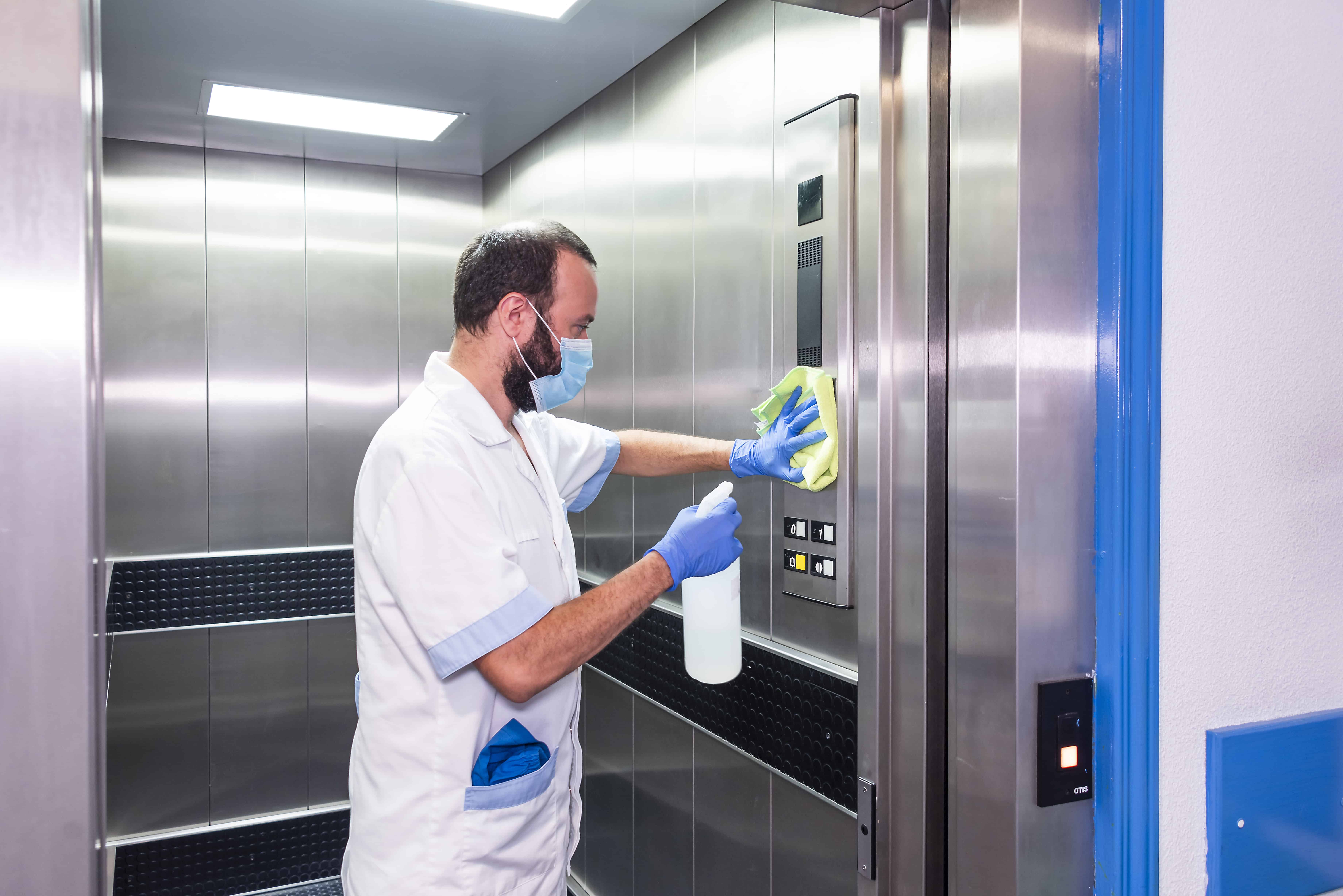 Day porter spraying and wiping down a high touch surface in an elevator.