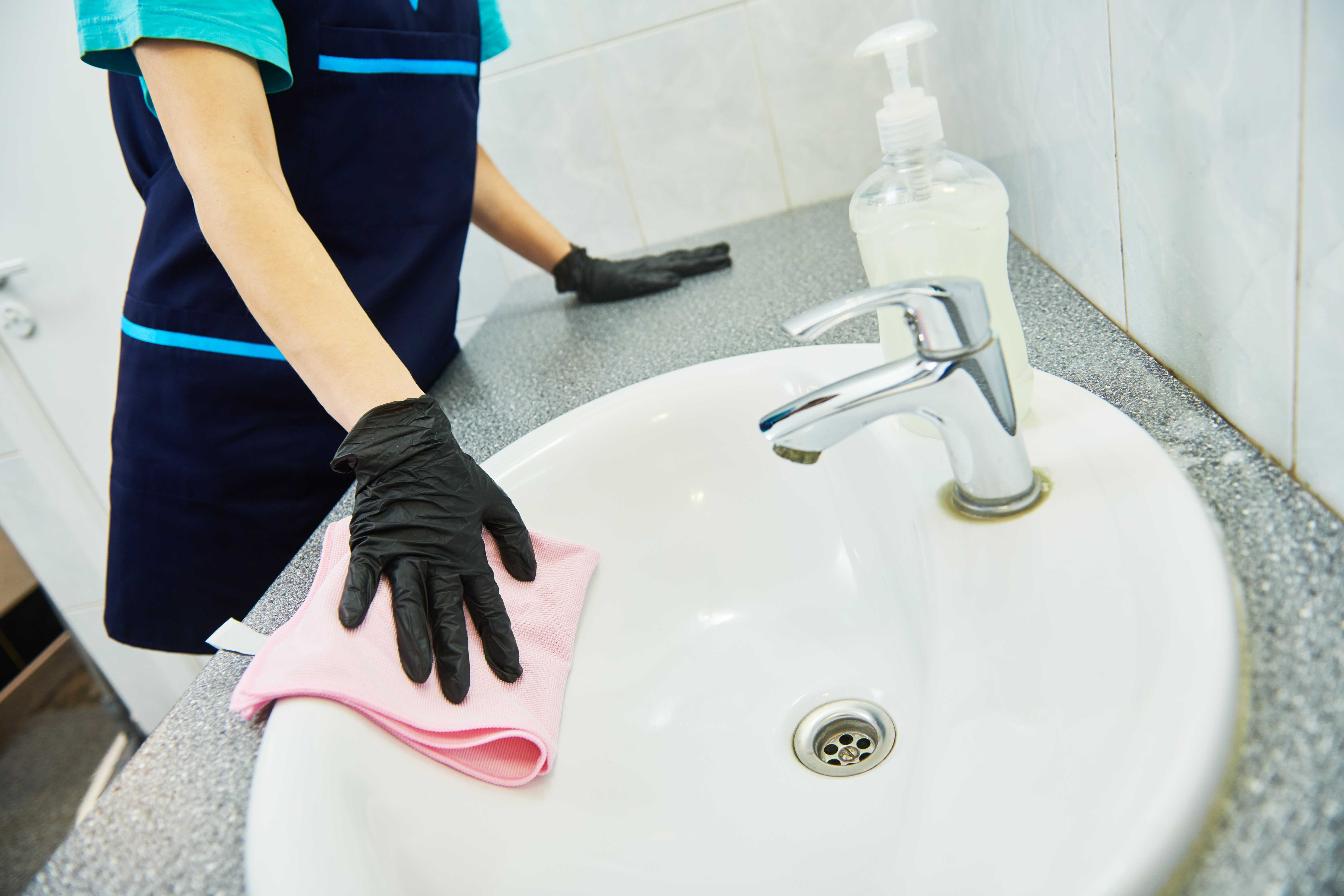 Day Porter wiping down facility sink with pink gloves