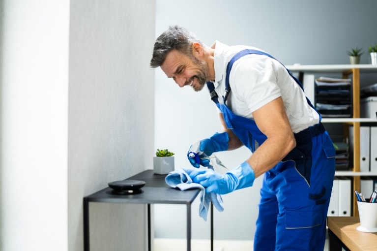 professional office cleaner wearing apron cleaning desk with microfiber 