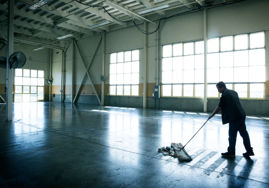 Industrial cleaning worker mopping floors in a large windowed commercial bay area